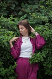 Young woman in vibrant pink outfit posing gracefully amidst lush bushes, Kharkiv, Ukraine.