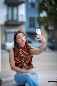 Trends in Women wear in 2026 Stylish woman taking a selfie outdoors with a smartphone in an urban setting.