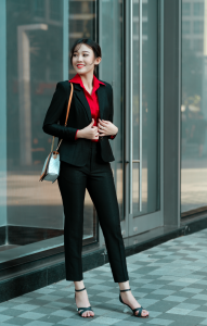 How to Choose Outfits You Can Wear on Different Occasions Smiling businesswoman in a black suit and red shirt standing outside a glass building.