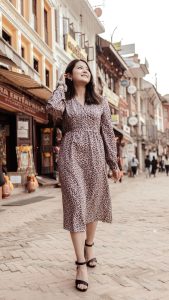 Smart Casual Style Guide for Women A smiling young woman in a polka dot dress strolls down a vibrant commercial street lined with shops, exuding confidence and style.