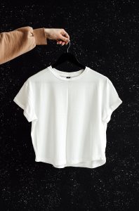 Smart Casual Style Guide for Women White t-shirt on hanger against a speckled black wall, showcasing minimalist fashion.