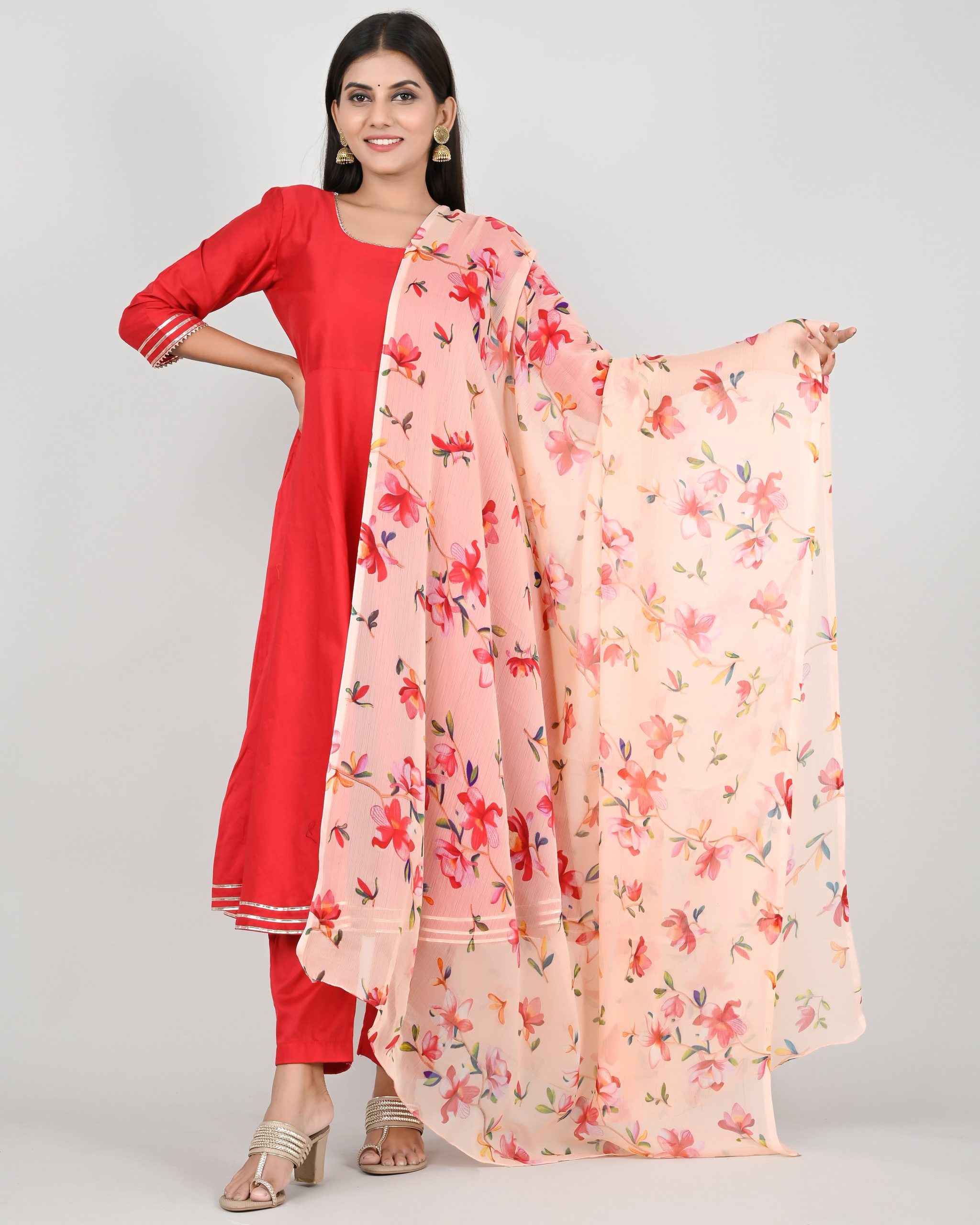 A woman in a red suit with a floral dupatta poses on a white studio background.