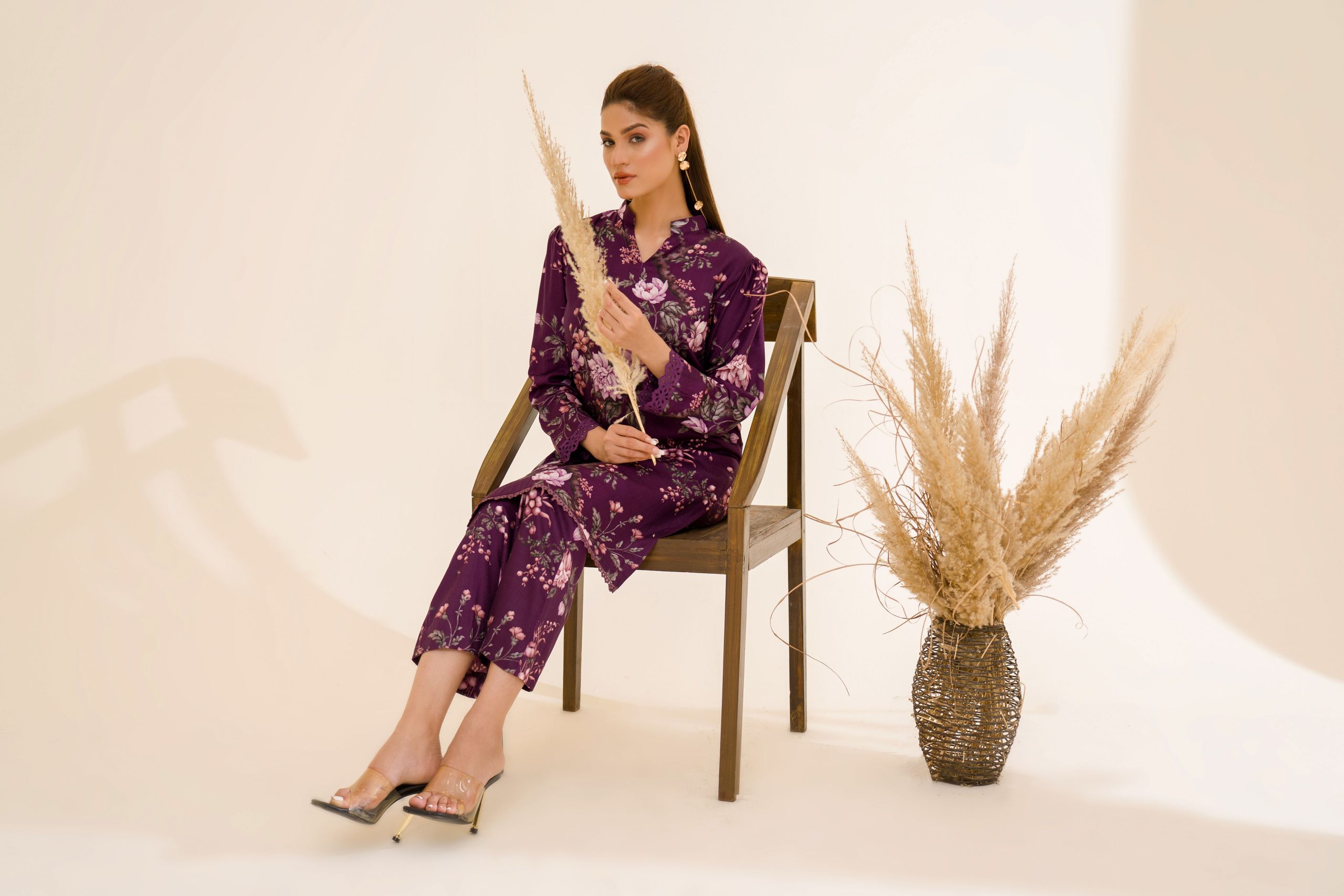 A fashion model in elegant floral attire posing with pampas grass indoors.